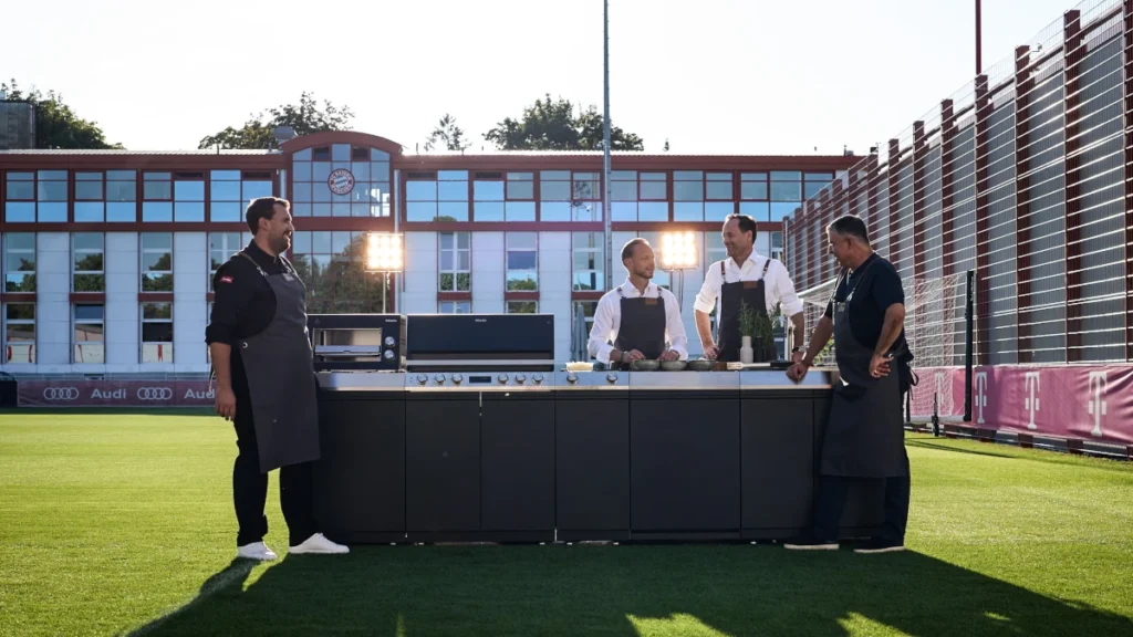 Kochen verbindet: Axel Kniehl (2. v. r.), Rouven Kasper (2. v. l.), Spitzenkoch Julian Resch (l.) und FC Bayern Legende Roy Makaay (r.) zusammen mit der neuen Miele Outdoor-Küche auf dem FC Bayern Trainingsgelände.